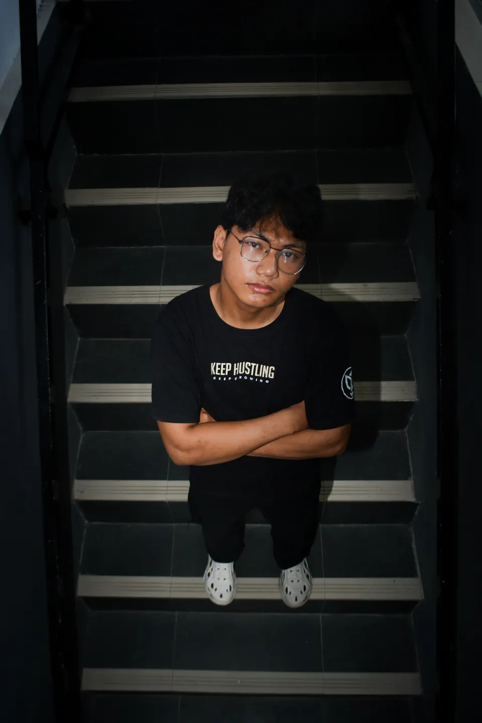 Portrait pria muda berkacamata duduk di tangga dari sudut atas, foto oleh Frazi