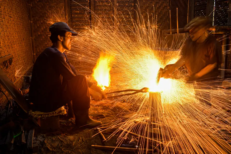 Foto dokumenter pandai besi menempa logam dengan percikan api, foto oleh Gio