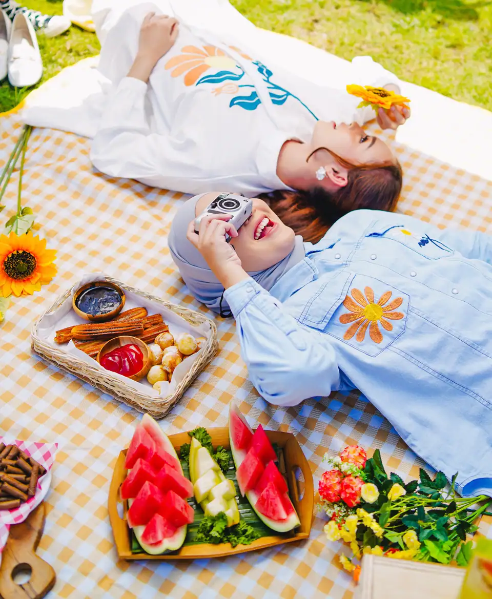 Foto konsep flat lay piknik: dua perempuan berbaring di samping semangka dan bunga, foto oleh Huda