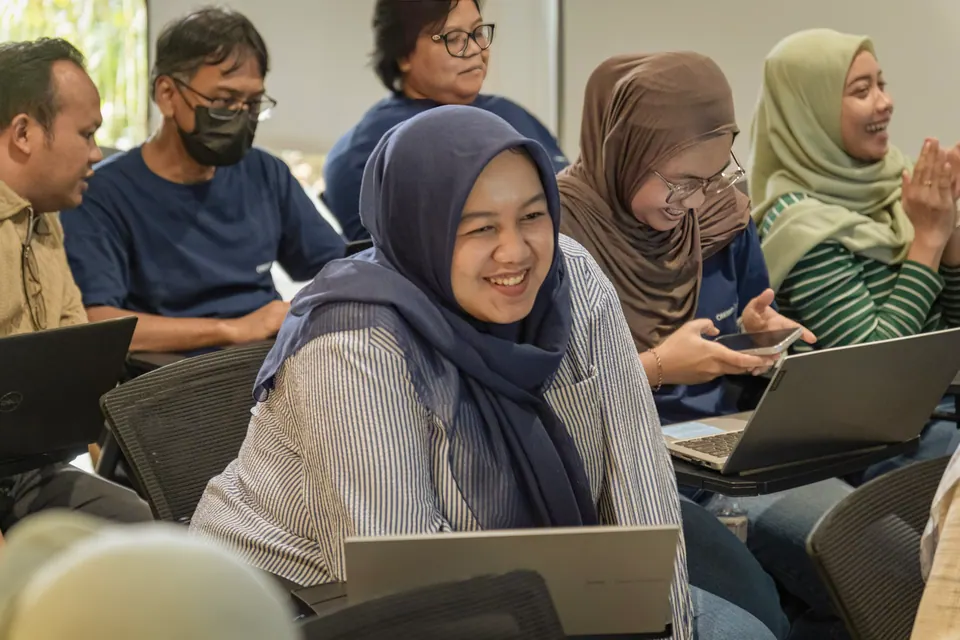Dokumentasi workshop: peserta tersenyum bekerja di depan laptop, foto oleh Ihir