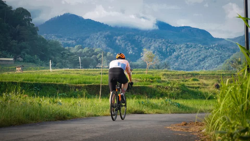 Foto olahraga outdoor: pesepeda melintas di jalan desa berlatar pegunungan, foto oleh Krisna
