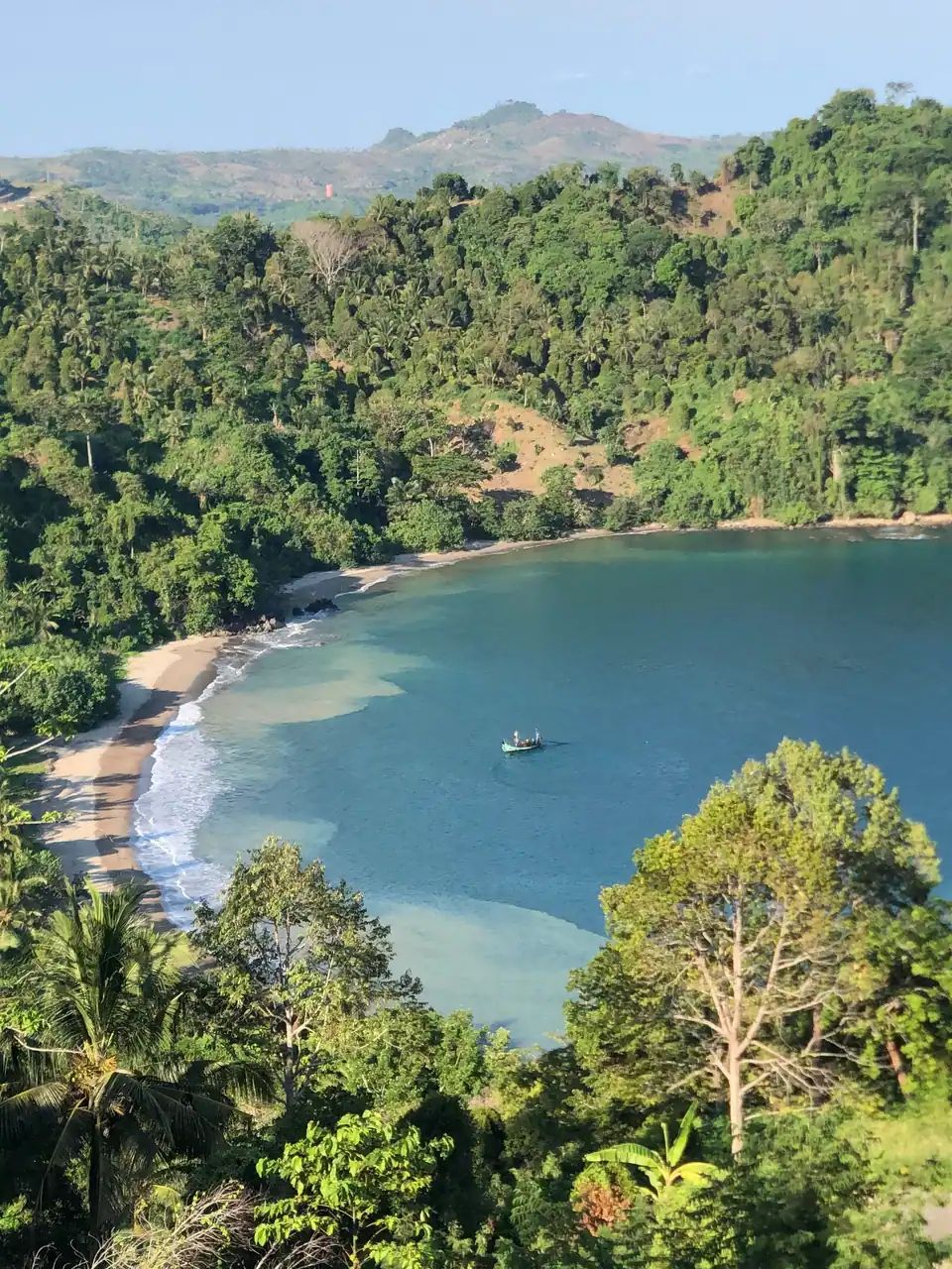 Foto lanskap teluk berair biru dikelilingi bukit hijau dari ketinggian, foto oleh Serena Pictures