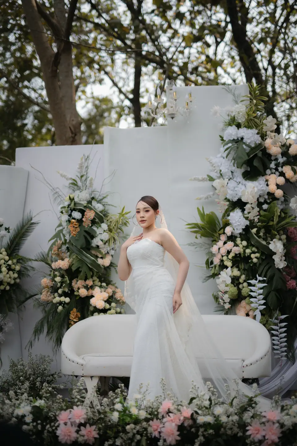 Foto pernikahan: pengantin perempuan bergaun putih di dekorasi bunga outdoor, foto oleh Yusron